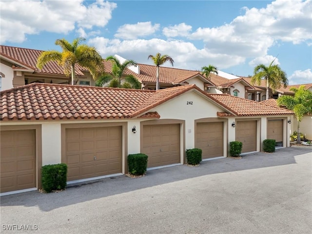 view of front of home with a tile roof, community garages, and stucco siding