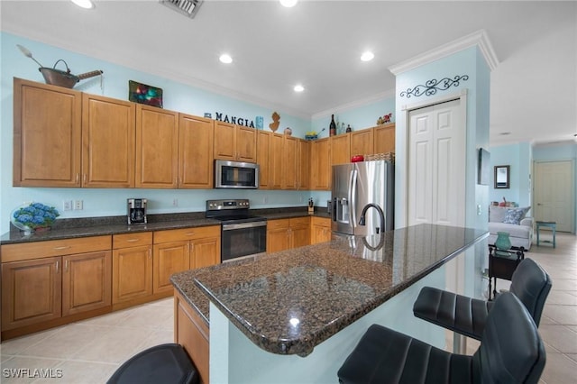 kitchen with stainless steel appliances, a kitchen island with sink, a breakfast bar, light tile patterned flooring, and ornamental molding