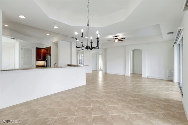 kitchen with ceiling fan with notable chandelier, a raised ceiling, light stone countertops, light tile patterned flooring, and stainless steel refrigerator