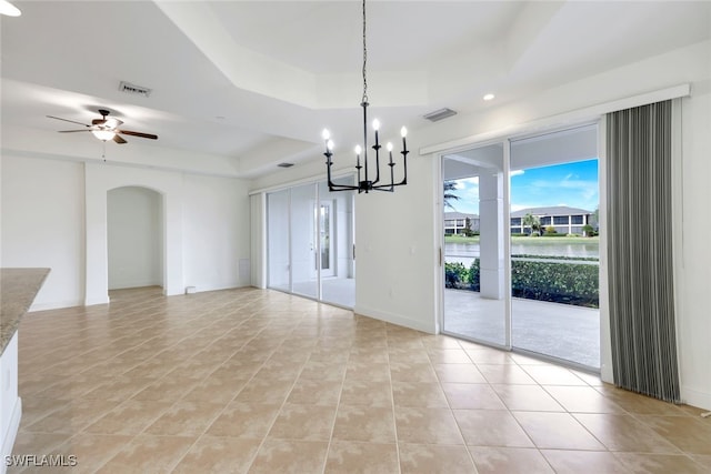 unfurnished dining area with light tile patterned floors, ceiling fan with notable chandelier, and a tray ceiling