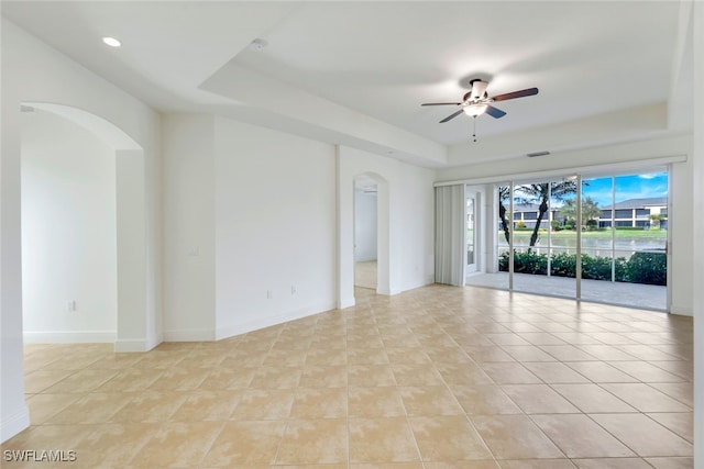 empty room with light tile patterned floors, a tray ceiling, and ceiling fan