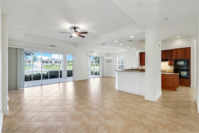 unfurnished living room featuring sink, ceiling fan with notable chandelier, a raised ceiling, and light tile patterned flooring