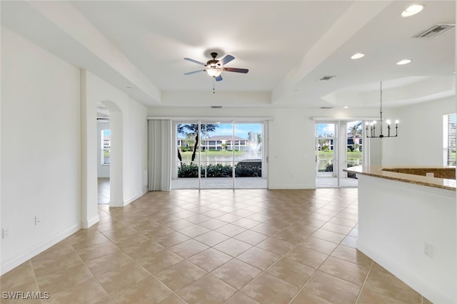 unfurnished living room featuring ceiling fan with notable chandelier, a tray ceiling, a wealth of natural light, and light tile patterned flooring