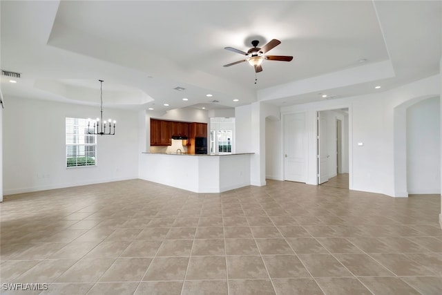 unfurnished living room featuring a tray ceiling, light tile patterned floors, and ceiling fan with notable chandelier