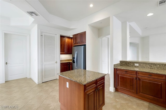 kitchen featuring a center island, stainless steel fridge, light tile patterned flooring, and light stone countertops