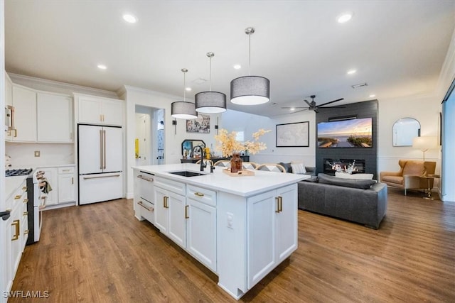 kitchen with white fridge, white cabinetry, an island with sink, and stainless steel range