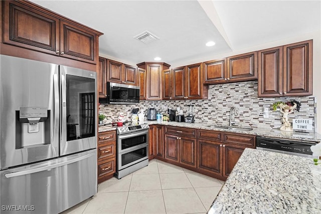 kitchen with decorative backsplash, appliances with stainless steel finishes, light stone countertops, sink, and light tile patterned floors