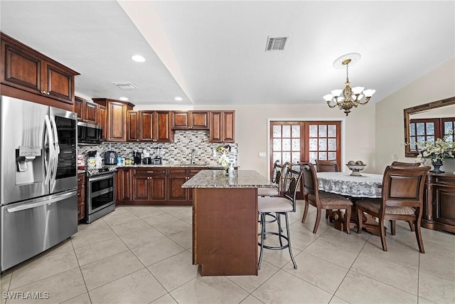 kitchen featuring a kitchen bar, appliances with stainless steel finishes, light stone counters, a chandelier, and hanging light fixtures