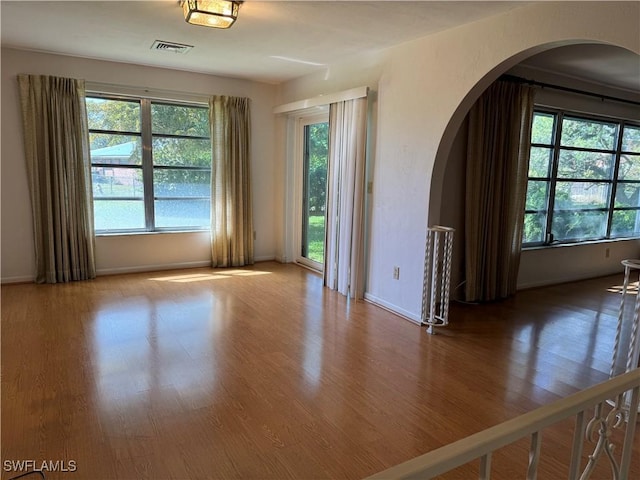 unfurnished room with a healthy amount of sunlight and hardwood / wood-style floors