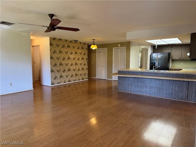 unfurnished living room featuring ceiling fan, sink, dark hardwood / wood-style flooring, and a skylight