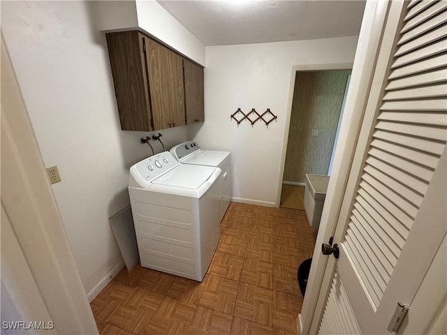 clothes washing area featuring cabinets, washing machine and clothes dryer, and light parquet floors