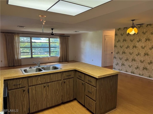 kitchen with sink, hanging light fixtures, kitchen peninsula, ceiling fan, and light hardwood / wood-style floors