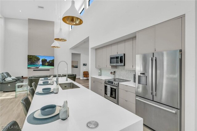 kitchen featuring decorative light fixtures, backsplash, sink, gray cabinetry, and stainless steel appliances