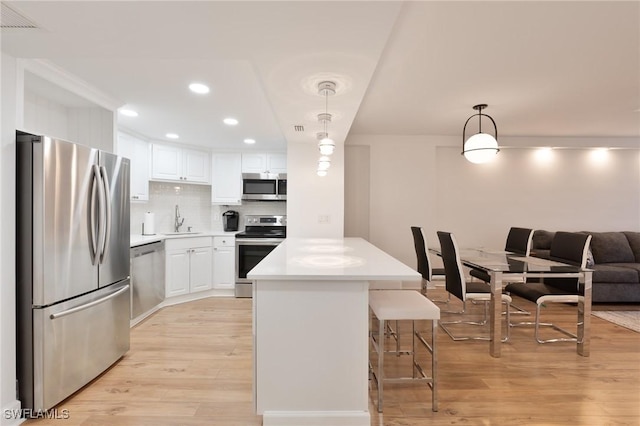 kitchen with a center island, sink, stainless steel appliances, decorative light fixtures, and white cabinets