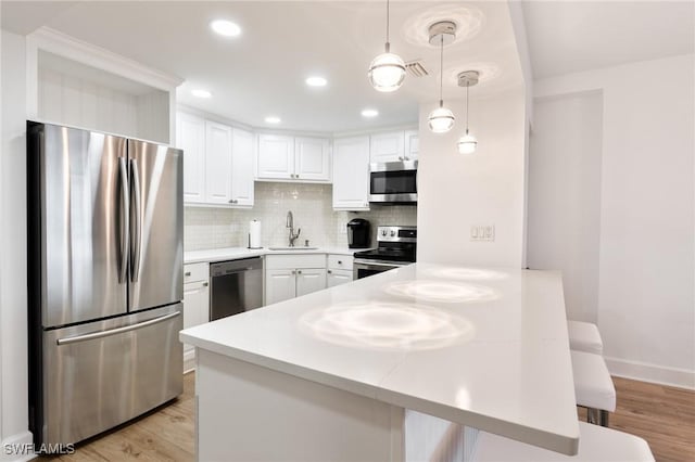 kitchen with decorative light fixtures, stainless steel appliances, white cabinetry, and light hardwood / wood-style flooring