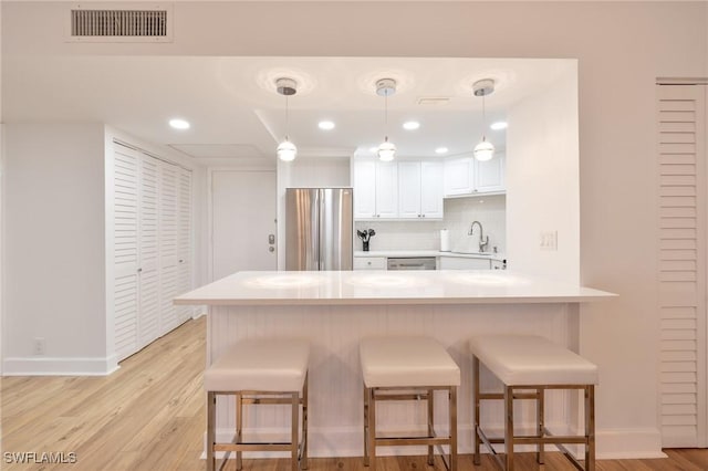 kitchen featuring a breakfast bar area, tasteful backsplash, white cabinetry, kitchen peninsula, and stainless steel appliances