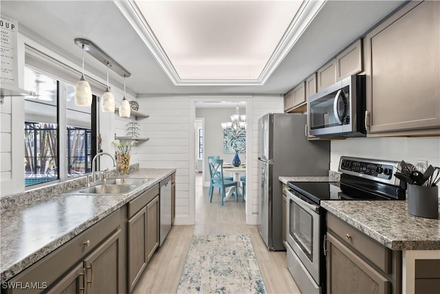 kitchen with appliances with stainless steel finishes, light wood-type flooring, a healthy amount of sunlight, sink, and a notable chandelier