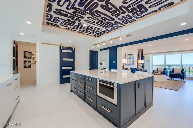 kitchen with a barn door, a tray ceiling, a kitchen island, and white cabinetry