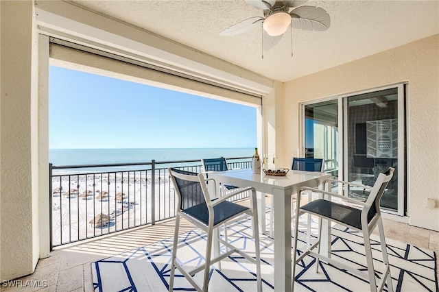 balcony with ceiling fan, a water view, and a view of the beach