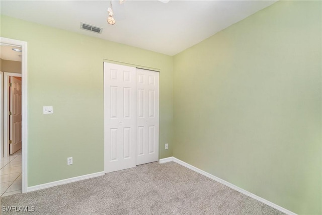 unfurnished bedroom featuring baseboards, a closet, visible vents, and light colored carpet