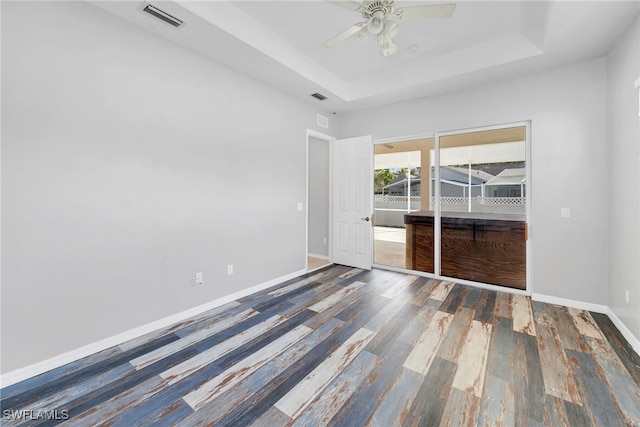 spare room with a tray ceiling, ceiling fan, and dark hardwood / wood-style flooring