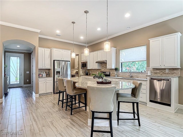20462 Misty Woods Ct, Estero, FL 33928 - kitchen featuring stainless steel appliances, arched walkways, a breakfast bar area, tasteful backsplash, and a kitchen island
