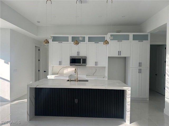 kitchen with pendant lighting, backsplash, sink, light stone countertops, and an island with sink