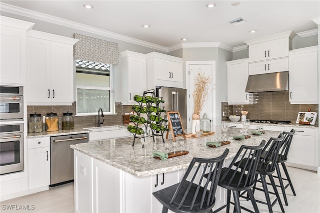 kitchen featuring a kitchen bar, a center island with sink, white cabinets, appliances with stainless steel finishes, and light stone counters