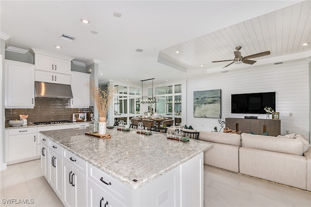 kitchen featuring light stone countertops, a center island, gas stovetop, and white cabinetry