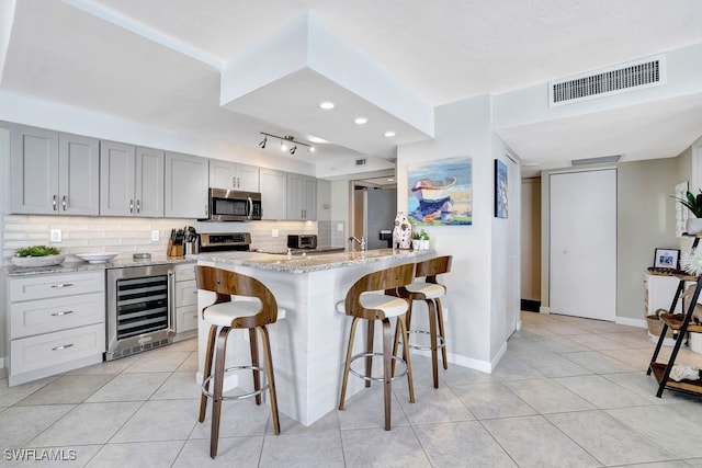 kitchen featuring light stone countertops, a kitchen breakfast bar, stainless steel appliances, gray cabinets, and wine cooler