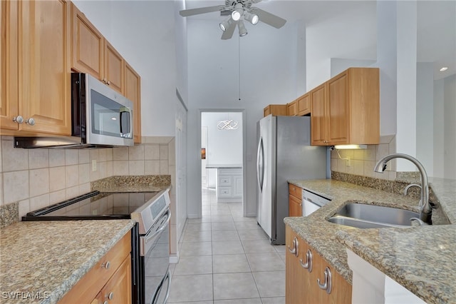 kitchen with appliances with stainless steel finishes, light tile patterned flooring, a sink, ceiling fan, and light stone countertops