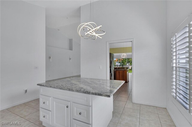 kitchen featuring light tile patterned flooring, pendant lighting, stainless steel fridge, white cabinets, and a chandelier