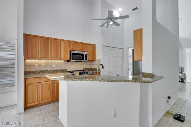 kitchen featuring light stone counters, stainless steel appliances, kitchen peninsula, and light tile patterned flooring