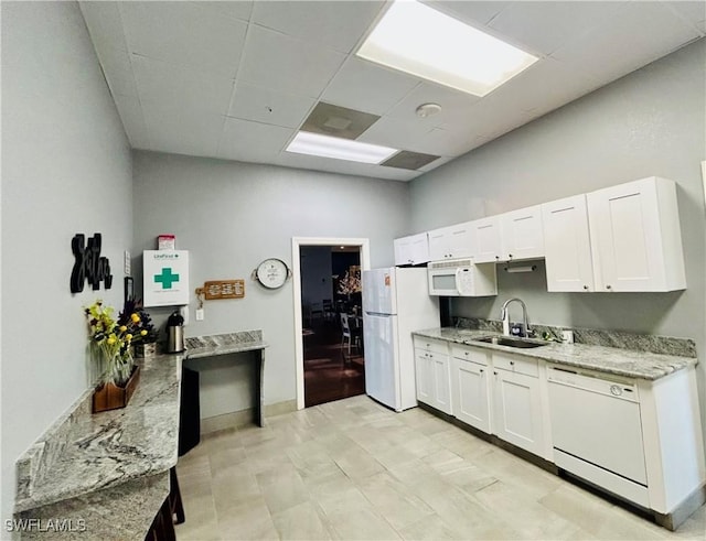 kitchen with white cabinets, a sink, light stone countertops, white appliances, and a drop ceiling