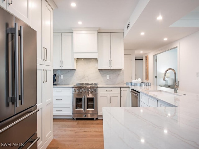 kitchen featuring sink, white cabinetry, premium appliances, light stone countertops, and custom range hood