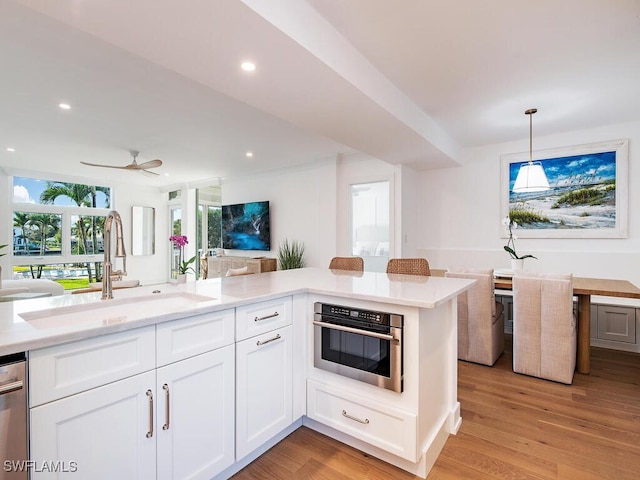 kitchen with sink, white cabinets, decorative light fixtures, oven, and light wood-type flooring