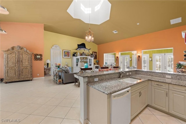 kitchen with white dishwasher, sink, vaulted ceiling with skylight, light tile patterned flooring, and light stone counters