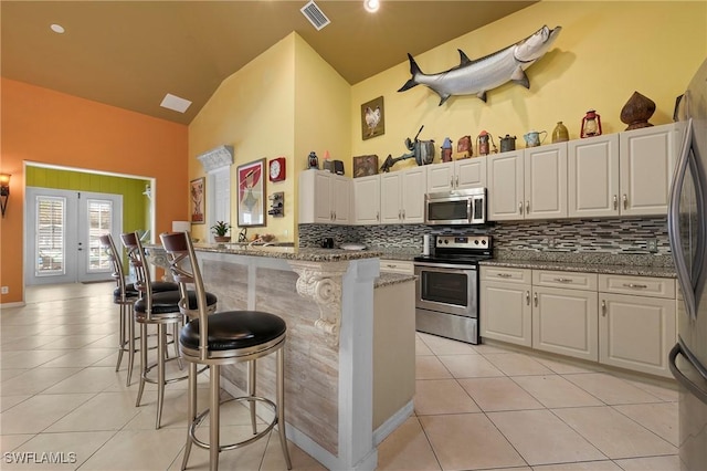 kitchen featuring french doors, a breakfast bar area, light stone counters, white cabinetry, and stainless steel appliances