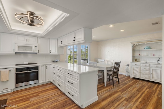 kitchen featuring stainless steel oven, kitchen peninsula, white cabinetry, and a tray ceiling