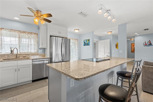 kitchen featuring white cabinetry, light stone countertops, a kitchen bar, a kitchen island, and appliances with stainless steel finishes