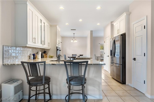 kitchen with white cabinets, kitchen peninsula, stainless steel fridge, and a breakfast bar