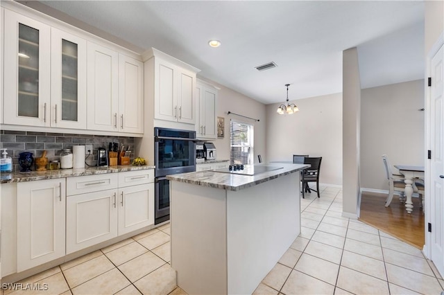 kitchen with light stone countertops, a kitchen island, white cabinetry, black electric stovetop, and light tile patterned floors