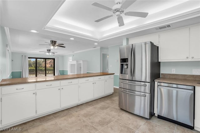 kitchen with a raised ceiling, stainless steel appliances, white cabinetry, and ornamental molding