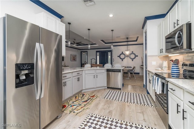 kitchen with stainless steel appliances, a raised ceiling, white cabinetry, and light hardwood / wood-style floors