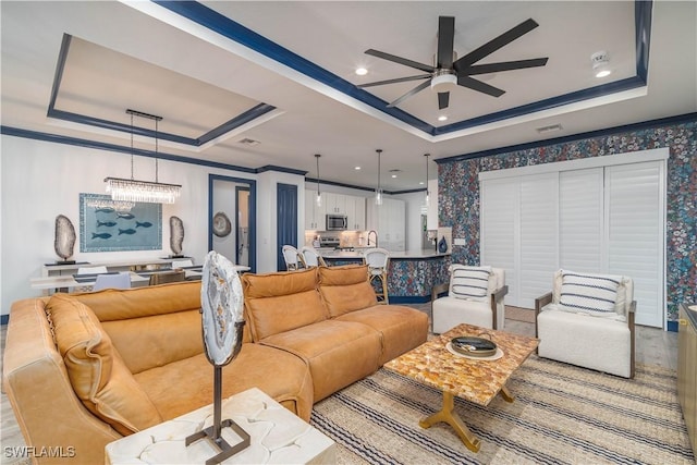 living room featuring a raised ceiling, crown molding, and ceiling fan with notable chandelier