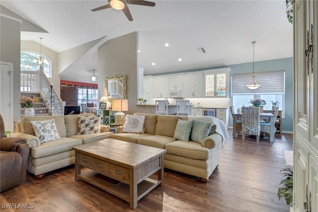 living room with ceiling fan with notable chandelier, dark wood-type flooring, and vaulted ceiling