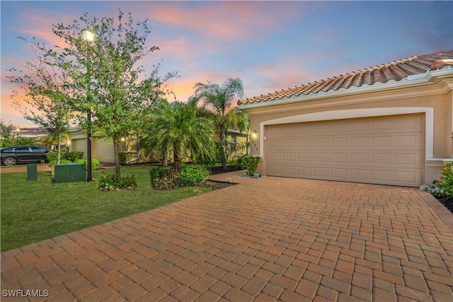 view of front facade featuring stucco siding, decorative driveway, a yard, and a tiled roof