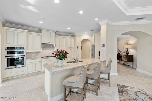 kitchen with sink, a breakfast bar area, stainless steel appliances, light stone countertops, and cream cabinetry