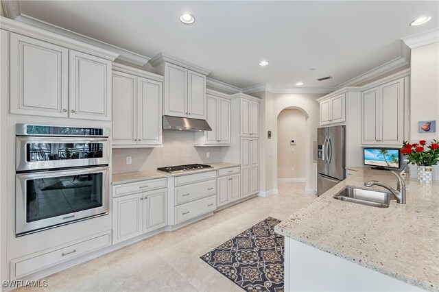 kitchen with white cabinetry, sink, light stone counters, stainless steel appliances, and crown molding