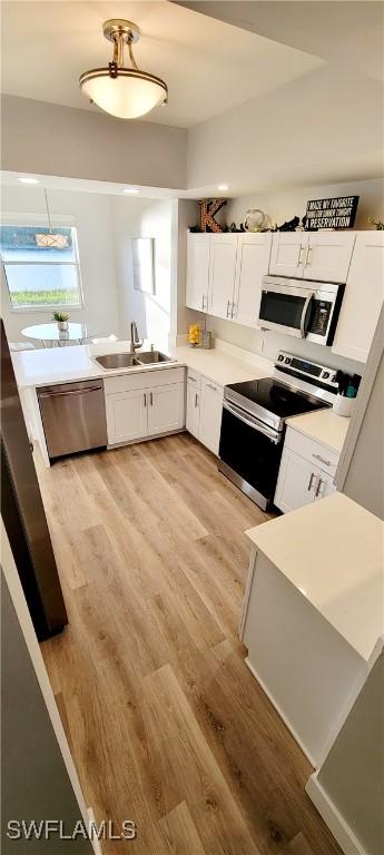 kitchen with white cabinetry, sink, stainless steel appliances, and light hardwood / wood-style flooring